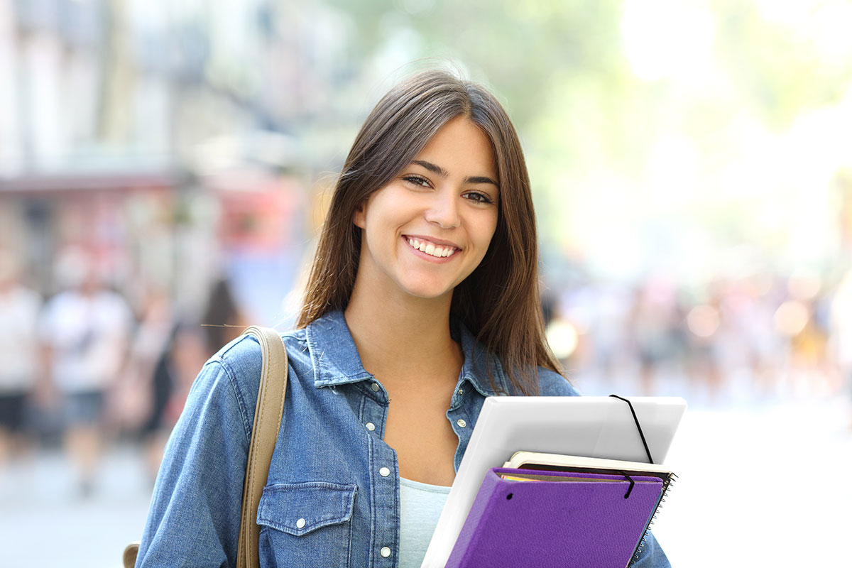 young student smiling at camera while holding notebooks